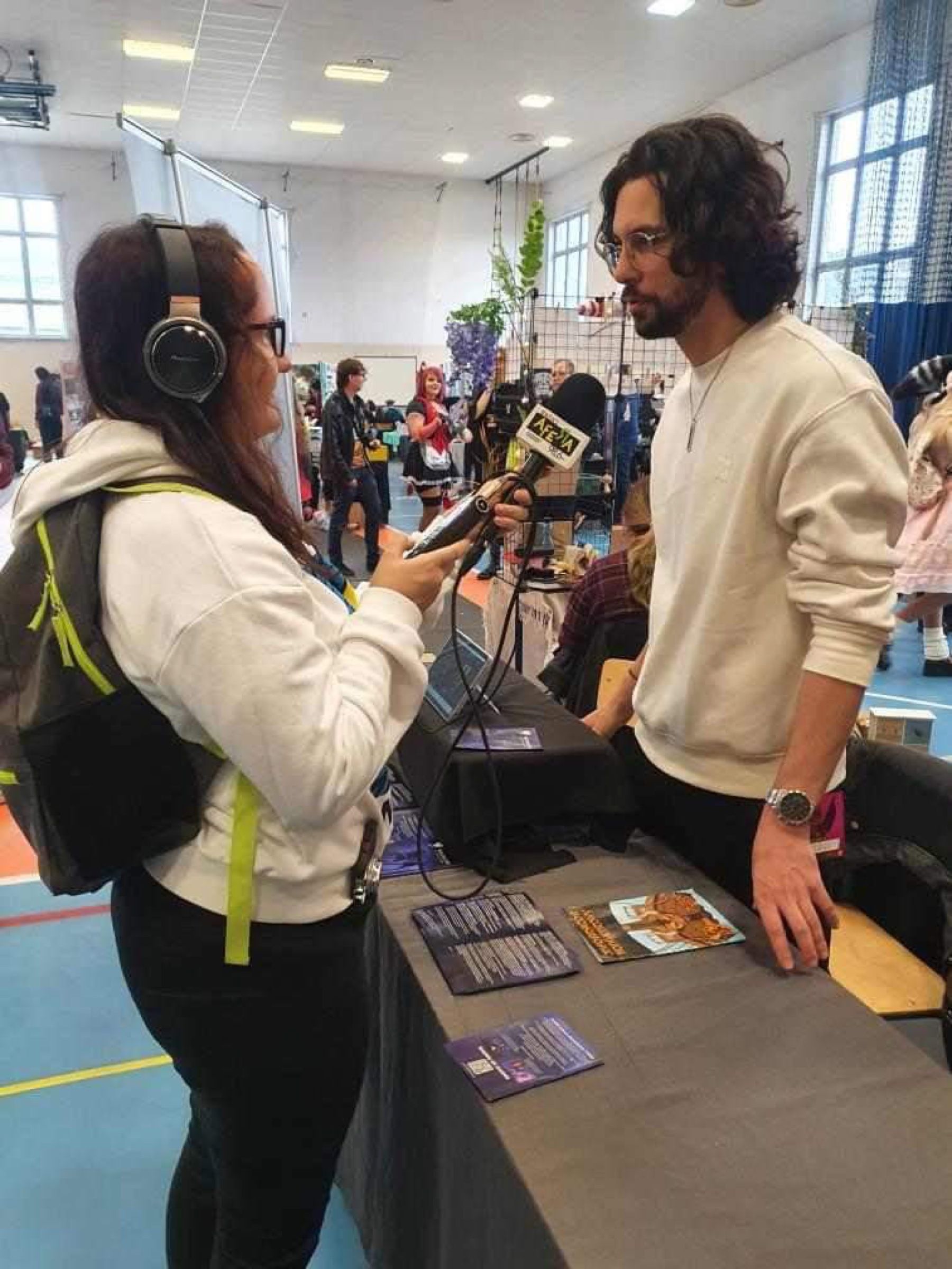 A radio reporter with headphones interviewing a team member at the convention stand.
